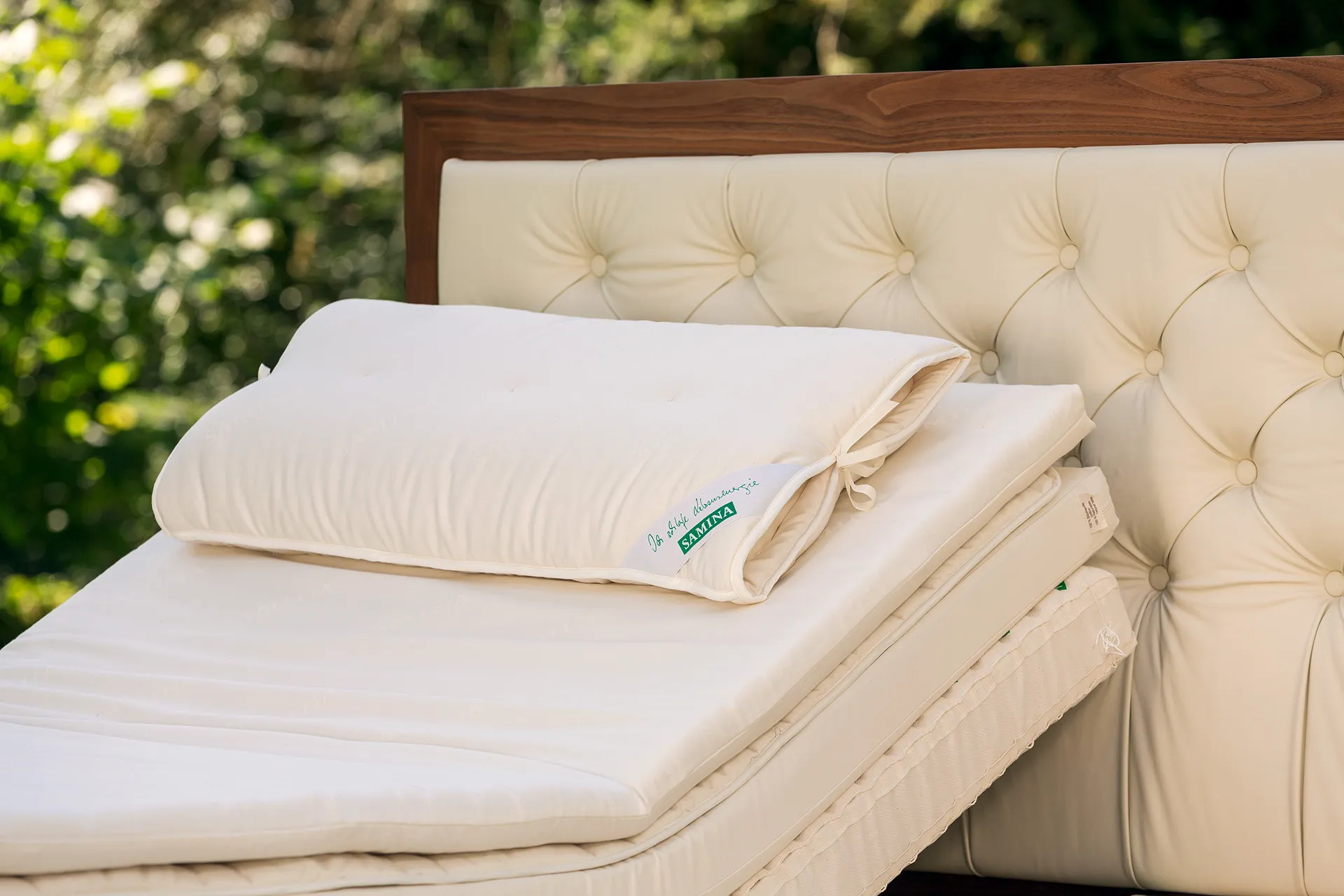 Bett mit gepolstertem Kopfteil und hellen Kissen in einem Garten Bett mit gepolstertem Kopfteil und hellen Kissen in einem Garten