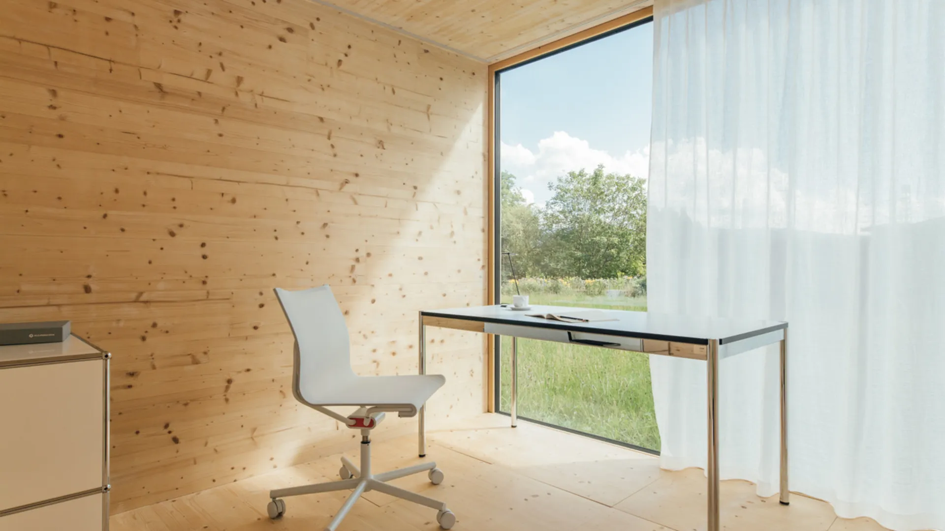 Schreibtisch und Drehstuhl vor einem großen Fenster in einem Holzraum Schreibtisch und Drehstuhl vor einem großen Fenster in einem Holzraum