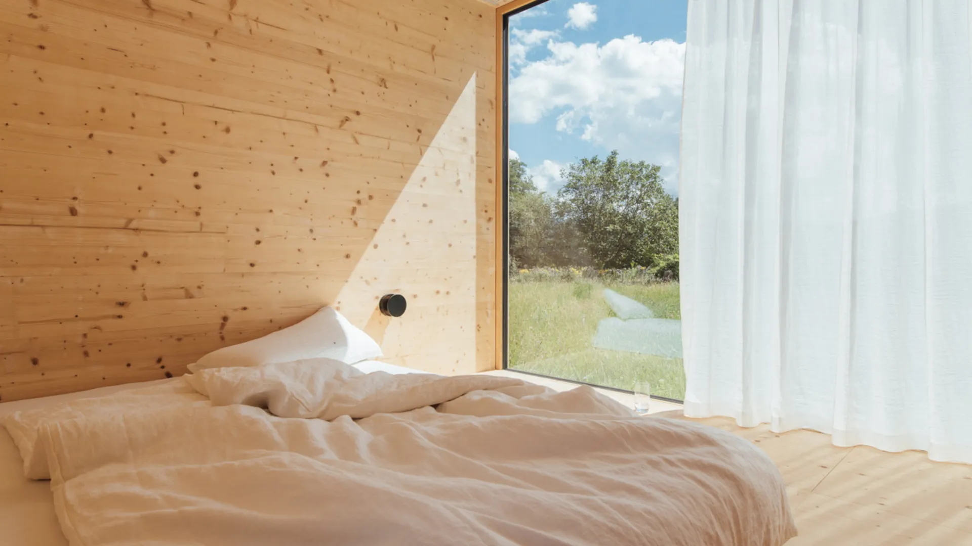 Bett in einem hellen Holzraum mit großem Fenster Bett in einem hellen Holzraum mit großem Fenster