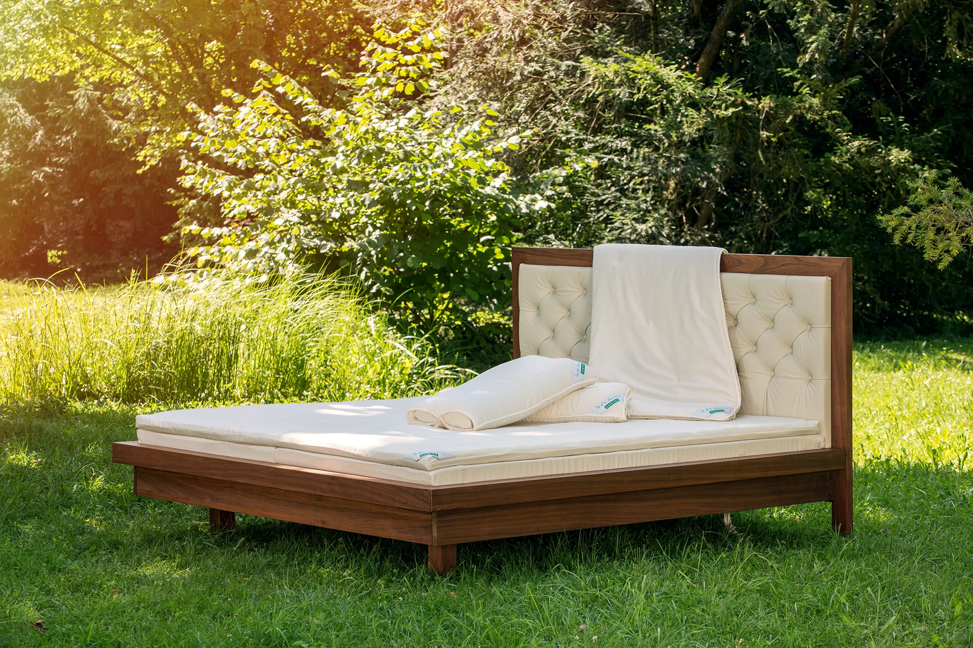 Bett mit gepolstertem Kopfteil und hellen Kissen in einem Garten Bett mit gepolstertem Kopfteil und hellen Kissen in einem Garten